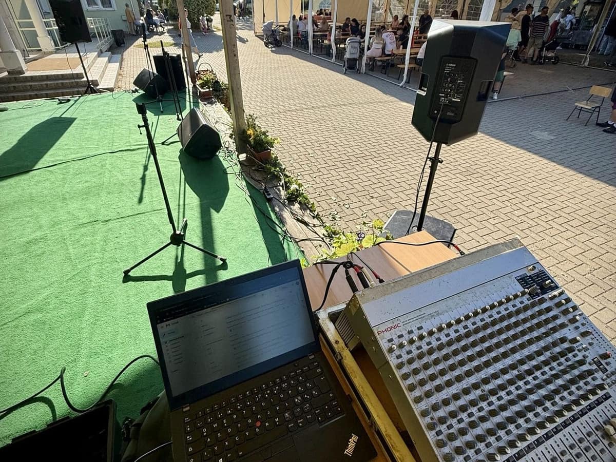 Keverőpult és laptop a szabadtéri falunapi színpad mellett, háttérben a közönség sátra